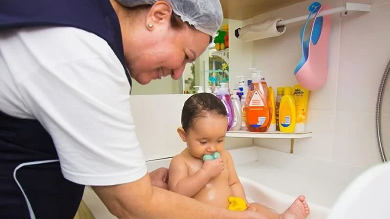 para  escolher um berçário é importante ter cuidadores atenciosos como esta devidamente equipada banhando um bebê