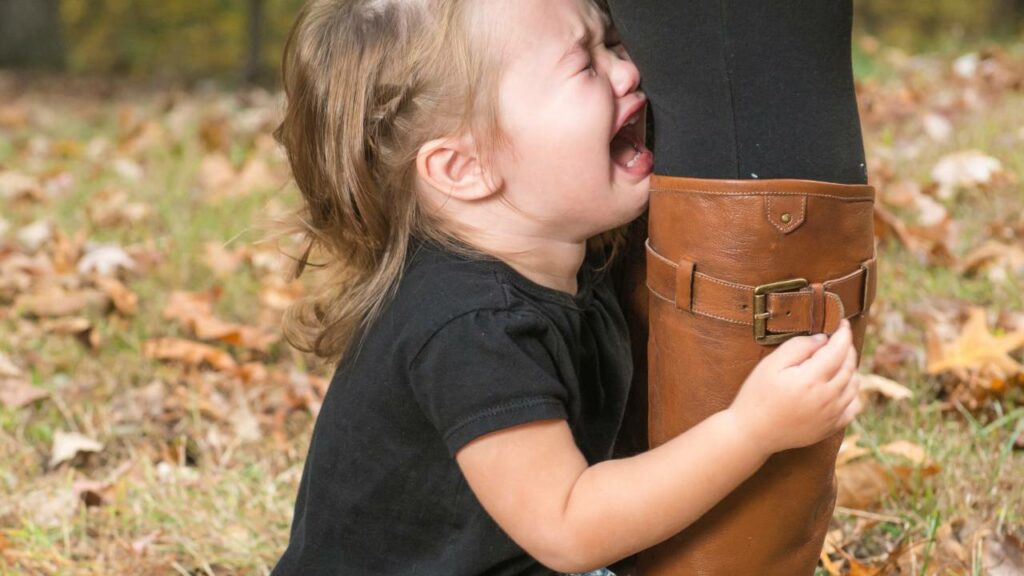 Criança chorando segurando a perna da mãe.