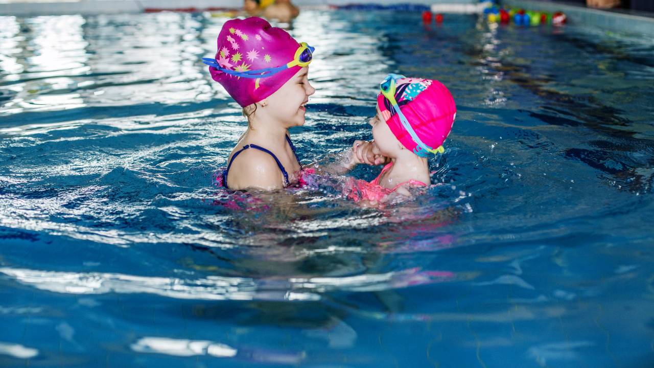Criança e bebê praticando aulas de natação infantil.