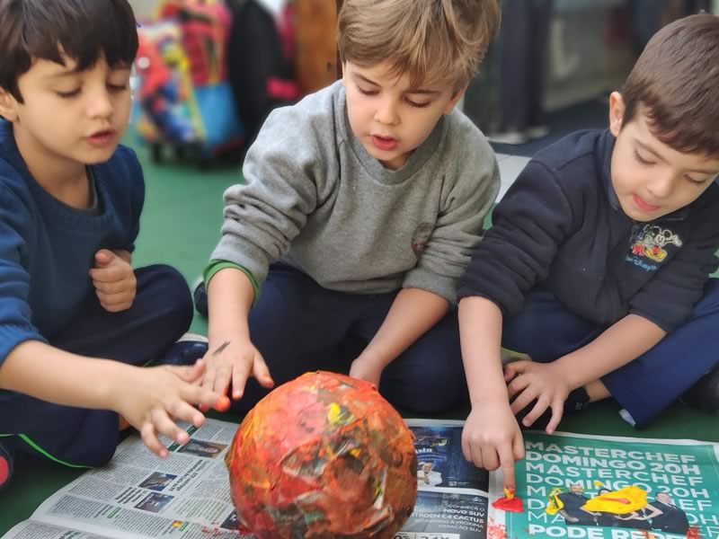 Crianças brincando com tinta e jornal na escola infantil