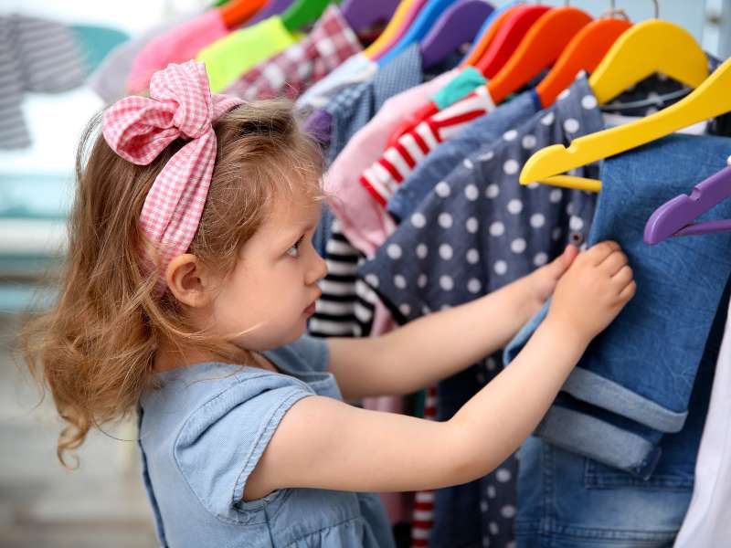 Garotinha procurando roupa em área dedicada às crianças em loja de roupas.