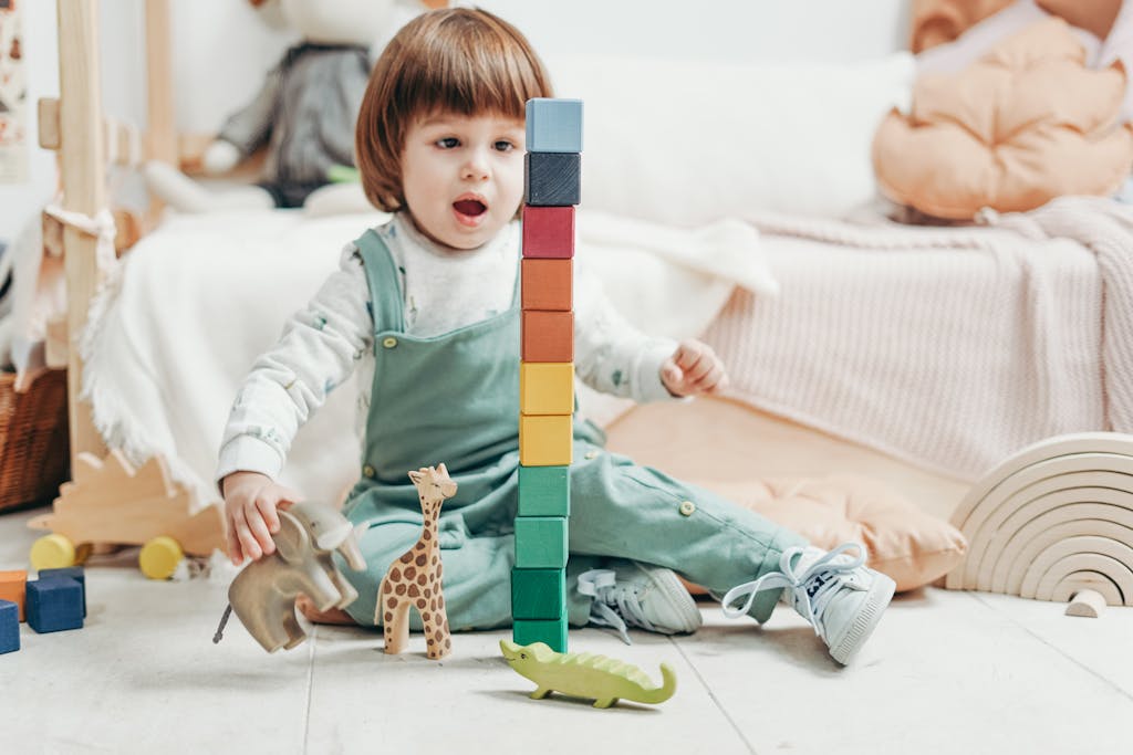 Criança adorável brincando com blocos de madeira coloridos e animais de brinquedo dentro de casa.