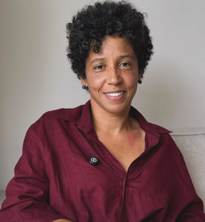 Mediadora do evento a frente de uma parede de fundo branco.