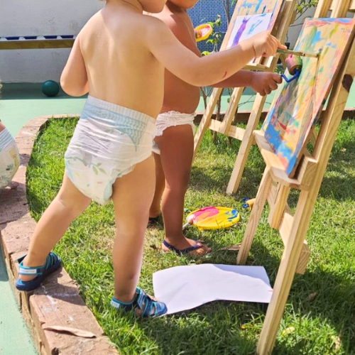 Duas crianças de fralda pintando um quadro na grama.